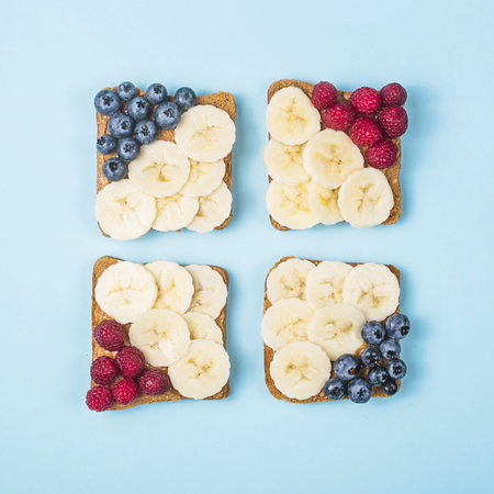 Healthy breakfast of sandwiches with peanut butter, banana and berries on a bright blue background....