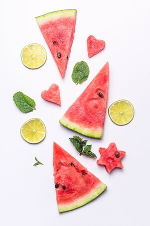 Red slices of ripe watermelon with mint leaves and lime slices on a white background. Top view, flat layの写真素材