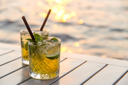 Two glasses of mojito with lime and mint on a white table of an outdoor cafe by the sea. Travel and...