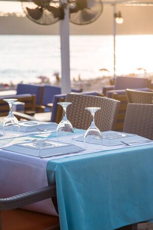 A cafe table by the sea is covered with a tablecloth and served with appliances and glasses in the sunlight. Travel, vacation and food conceptの写真素材