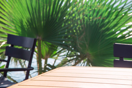 Table of a street coffee shop near the green branches of palm trees. Mock up for business in travel,...