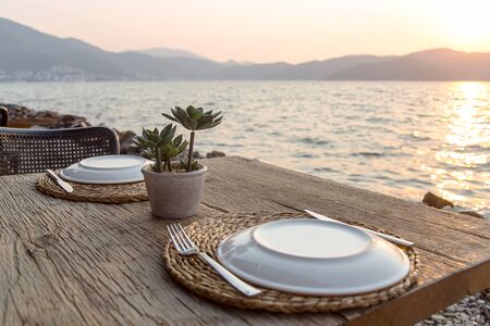 Beautiful served table of a modern cafe by the sea with dishes and flowers. Stylish restaurant for dinner on vacationの写真素材