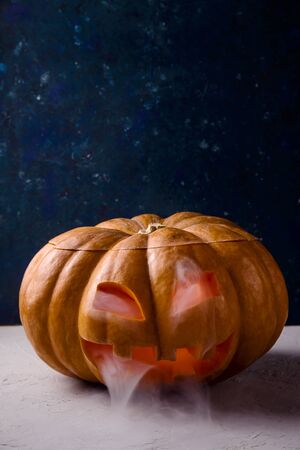 A large pumpkin with a carved face as a symbol of Halloween with white smoke from it on a blue backgroundの写真素材