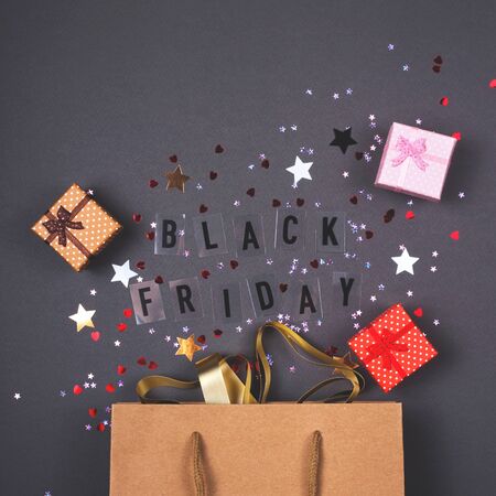 Kraft paper bag on bright dark background. With gift boxes and confetti. Black friday is written.の写真素材