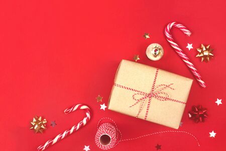 Christmas gift in a craft wrapper among bows, stars and candies on a bright red background with copyspace.の写真素材