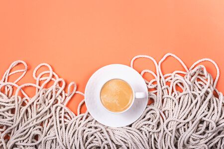 Cotton white rope texture as natural material with cappuccino in a white cup on a bright pink coral background with copy space. Top view, flat lay.の写真素材