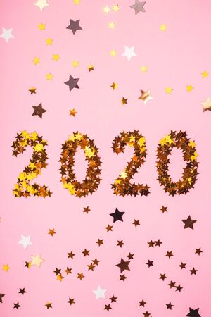 The numbers 2020 are laid out from golden glowing stars on a bright pink background among different stars. Winter holidays and christmas overlay. Top view, flat lay.の写真素材