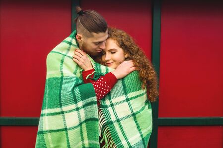 Beautiful young guy and girl cuddling in a green plaid and Christmas colors on a red background.の写真素材
