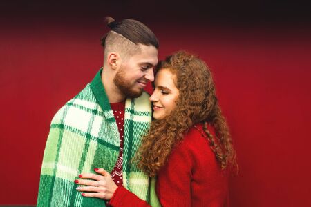 Beautiful young guy and girl cuddling in a green plaid and Christmas colors on a red background.の写真素材