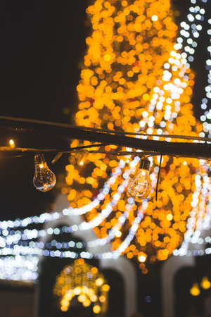 A garland of yellow incandescent lamps as an urban decoration for the Christmas holidays. Lights and Christmas tree on the background.の写真素材
