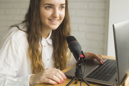 Girl records a podcast with a microphone at home. Modern technologies for creating content for bloggers and influencers.の写真素材