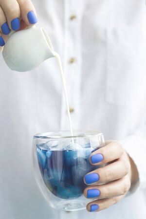 Blue matcha cold drink with ice in a glass beaker in the hands of a woman with blue manicure. Color of the year 2020 trendの写真素材
