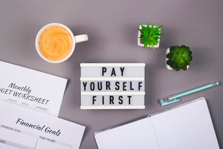 Pay yourself first. It is written on a decorative panel on the gray workplace of a freelancer who...