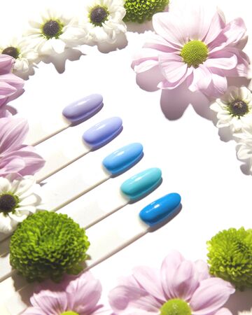 Examples of different bright spring colors of nail polish for manicure on plastic tips next to flowers. Isolate on a white background.の写真素材