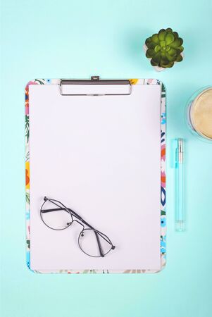Blank paper on colored clipboard with copy space on a bright neo-mint background with glasses and succulents. Top view, flat lay.の写真素材