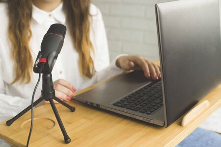 Girl records a podcast with a microphone at home. Modern technologies for creating content for bloggers and influencers.の写真素材