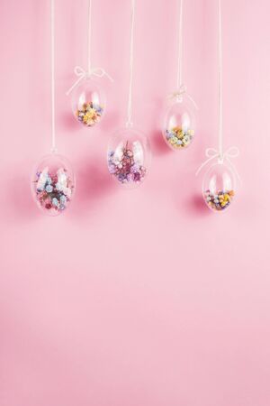 Easter eggs are transparent and filled with small colorful flowers hanging on a rope on a pink background. Minimalistic holiday decoration.の写真素材