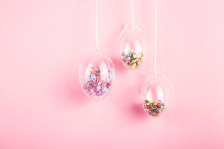 Easter eggs are transparent and filled with small colorful flowers hanging on a rope on a pink...