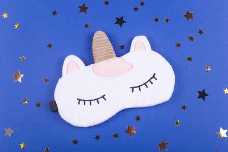 Sleeping mask in the shape of a unicorn on a blue background among the stars. Healthy sleep concept. Top view.の写真素材