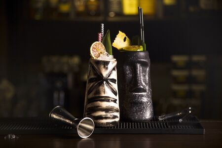 Tiki Drink Cocktails. Two cocktails in different glasses against the background of a bar decorated with dried fruits and tropical leaves.の写真素材