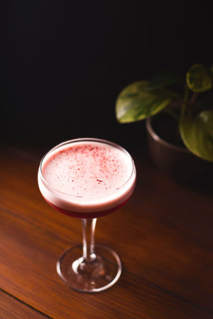 Raspberry smoothie with foam and berry crumbs in a glass on a wooden table in a dark bar.の写真素材