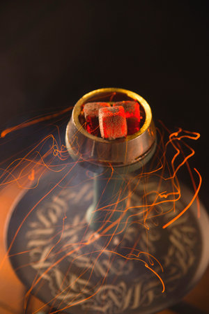 Red sparks from the hookah coals flying around the bulb. Smoking hookah in a bar concept.