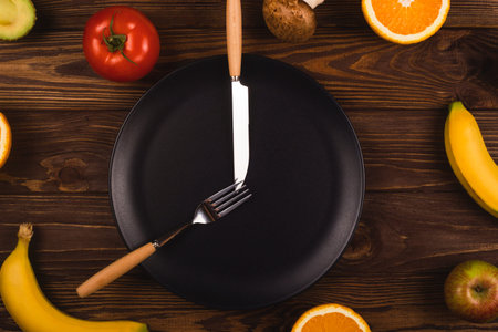 Black plate on a wooden table among fruits and vegetables. Vegetarianism and intermittent fasting...