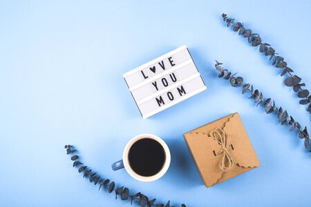 Mom love you written on a decorative panel next to a cup of coffee and eucalyptus on a blue background.の写真素材