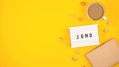 Abbreviation word JOMO written on a decorative board on a bright yellow background. The concept of relaxation from information and gadgets. Top view, flat lay, copy space.の写真素材