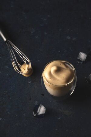 Homemade dalgona coffee made of instant coffee, sugar and milk on a dark background with ice.の写真素材