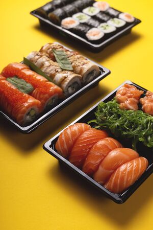 Sushi with fresh fish salmon and eel delivery in containers to the house on a bright yellow background.の写真素材