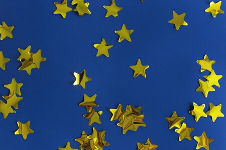 Gold shiny sweets in the shape of stars on a bright blue background. Festive and Christmas background. Top view, copy spaceの写真素材