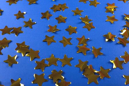 Gold shiny confetti in the shape of stars on a bright blue background. Festive and Christmas background. Top view, copy spaceの写真素材