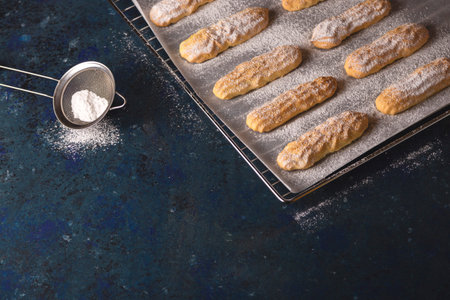 Homemade Savoyardi cookies on a baking sheet on a blue background. Top view, flat lay.