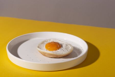 Fried egg on a round plate on a yellow table with hard shadows. The concept of creativity and minimalism in cooking.の写真素材