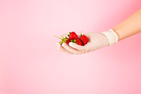 Hand in glove holds strawberries on a pink background.