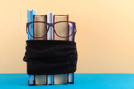 A stack of books with glasses and a protective black mask against the virus, social distance and medical recommendations for dealing with a pandemic in school.の写真素材
