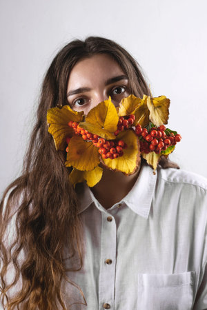 Woman in mask of autumn leaves and berries. Health care concept during pandemic