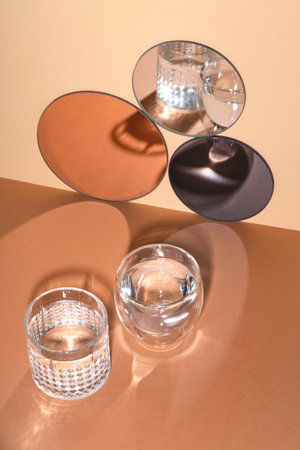 Two glasses of water with shadows next to round mirrors