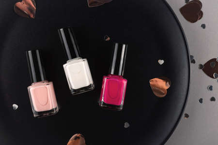 Three different colors of nail polishes on a dark stylish background with confettiの写真素材