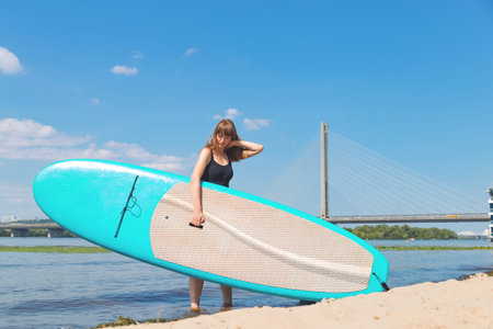 A beautiful woman is engaged in summer active sports on the river on a SUP board