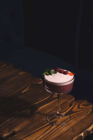Raspberry cocktail sour in a dark bar on a wooden tableの写真素材