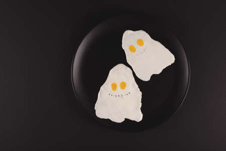 Fried eggs in the shape of halloween ghosts on black backgroundの写真素材
