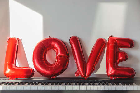 Red balloons in the shape of the word love on a home pianoの写真素材