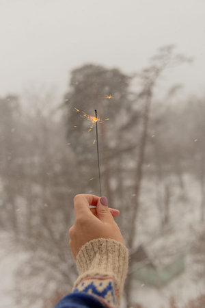 Womans hand holds sparkle during snowfall against town