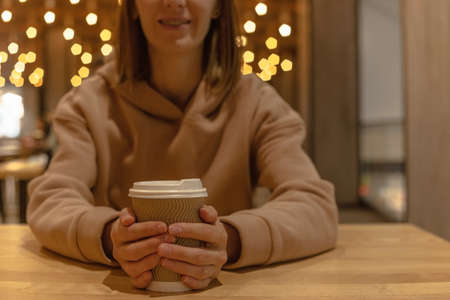 A cup of coffee in the hands of a girl sitting at a table on a food courtの写真素材