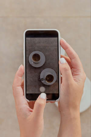 Woman photographing cups of coffee on smartphoneの写真素材