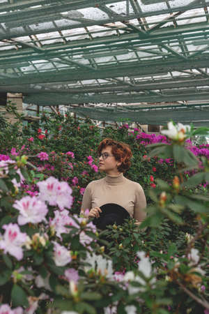 A beautiful plus size girl in a hat smiles among the green plants of greenhouseの写真素材