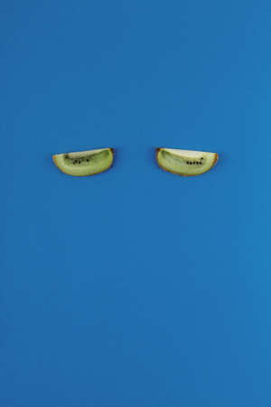 Kiwi slices like eyes on a blue background. Food concept for sleep and insomnia treatmentの写真素材