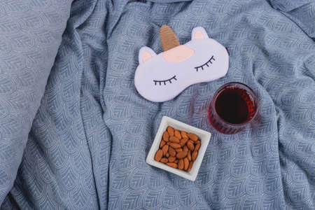 Cherry juice and almonds for healthy sleep on the bed next to a sleep mask.の写真素材